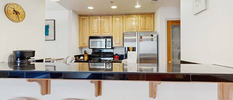 A modern kitchen with wooden cabinets, a stainless steel refrigerator, a microwave, and a large island with stools.