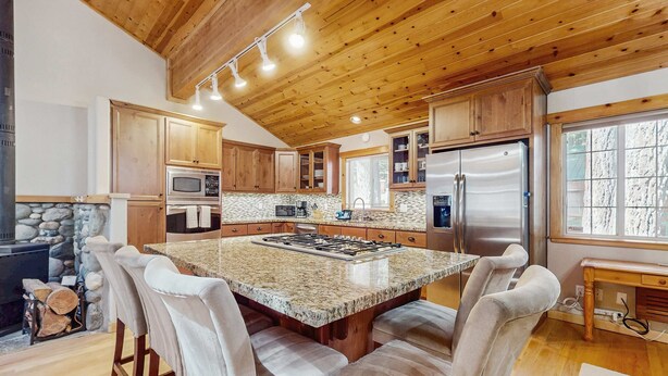 A kitchen with wooden cabinets, a granite island, and a stone fireplace. - Updated Cabin with Deck, Grill, Washer and Dryer, Access to Pool, Spa (Truckee)