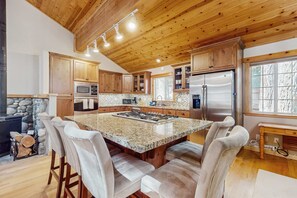 A kitchen with wooden cabinets, a granite island, and a stone fireplace. - Updated Cabin with Deck, Grill, Washer and Dryer, Access to Pool, Spa (Truckee)
