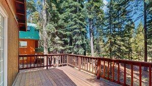 A wooden deck with a railing, surrounded by tall trees. - Updated Cabin with Deck, Grill, Washer and Dryer, Access to Pool, Spa (Truckee)