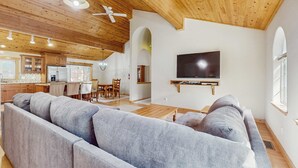 A modern living room with a large gray sectional sofa, wooden ceiling, and a flat-screen TV mounted on the wall. - Updated Cabin with Deck, Grill, Washer and Dryer, Access to Pool, Spa (Truckee)