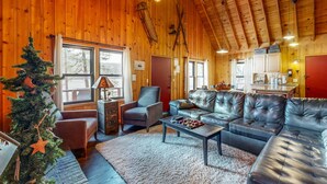Un interior de cabaña acogedor, con detalles de madera, sofás de cuero, chimenea y un árbol de Navidad.
