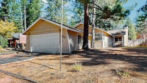 A two-story house with a garage, surrounded by pine trees and a clear sky. - Charming Pet Friendly Home with Hot Tub, Enclosed Yard, Short Walk to Beach (South Lake Tahoe)