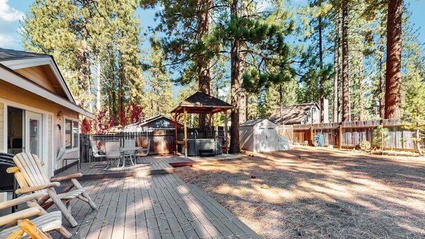 A wooden deck with outdoor furniture, a gazebo, and a cabin-like structure in a forested area. - Charming Pet Friendly Home with Hot Tub, Enclosed Yard, Short Walk to Beach (South Lake Tahoe)