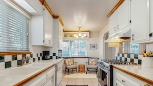 A kitchen with white cabinets, a gas stove, a sink, and a window with blinds. - Charming Pet Friendly Home with Hot Tub, Enclosed Yard, Short Walk to Beach (South Lake Tahoe)