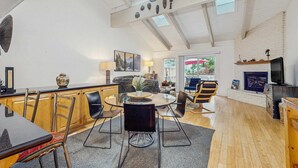 Een ruime woonkamer met een hoge plafond, een open haard en een eettafel met stoelen.