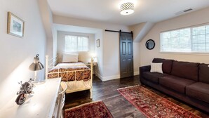Ein Schlafzimmer mit Bett, Schminktisch, Motorrad, Schreibtisch, Lampe, Sofa und einer Tür.