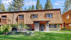 A two-story wooden house with a stone entrance, a well-maintained lawn, and a view of tall trees. - Family-Friendly townhouse near lake - convenient & walkable location (Incline Village)