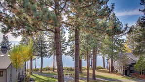 A residential area with tall pine trees, a pathway, and a lake in the background. - Comfortable Townhome with Pool, Deck, & Lovely Sunsets - Walk to Lake (Kings Beach)