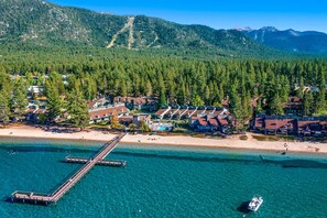 An aerial view of a coastal resort with a pier, clear turquoise waters, and a backdrop of dense forested mountains. - Tranquil townhome with picturesque lake views and an abundance of amenities (South Lake Tahoe)