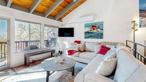 A spacious living room with a high ceiling, a large sofa, a coffee table, and a painting of a boat on the wall. - Condo near Lake Tahoe with pool, hot tub, grill, & wood fireplace - sleeps 6 (Stateline)