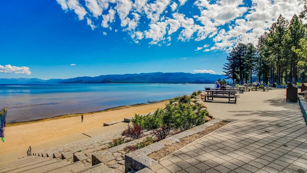 A beach with a paved walkway, benches, and trees. - Condo near Lake Tahoe with pool, hot tub, grill, & wood fireplace - sleeps 6 (Stateline)