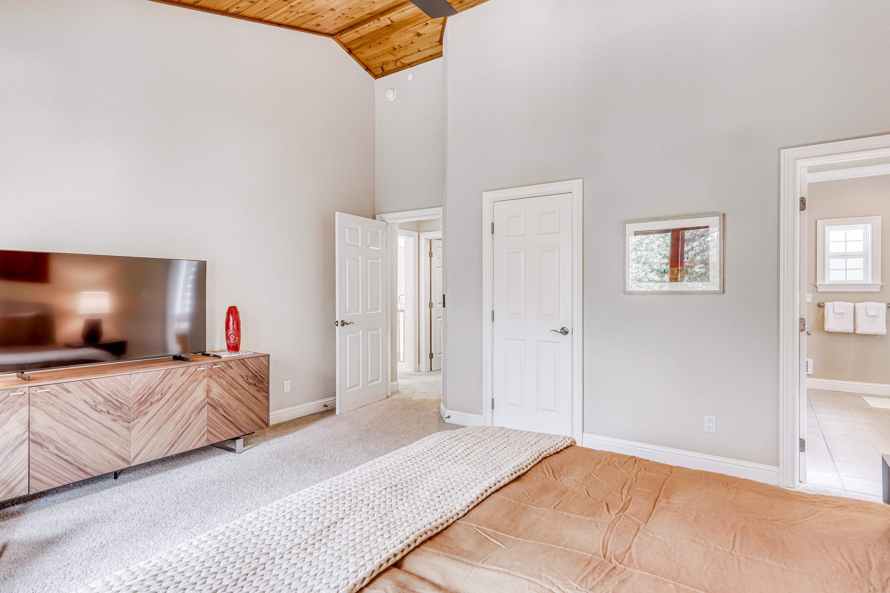 A modern room with a wooden ceiling, a flat-screen TV, a beige sofa, and a white rug.