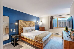 Une chambre à coucher avec un lit en bois, une table de chevet, une chaise, un bureau avec des livres, un miroir et une fenêtre donnant sur une clôture.