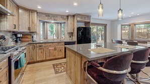 A modern kitchen with wooden cabinets, a central island, bar stools, and a large window. - Beautiful home with private hot tub, gazebo, and gas fireplace (South Lake Tahoe)