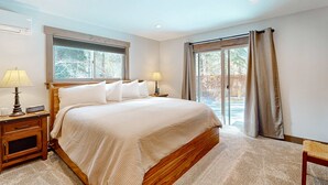 A bedroom with a large bed, two bedside tables with lamps, a window, and a sliding glass door leading to an outdoor area. - Beautiful home with private hot tub, gazebo, and gas fireplace (South Lake Tahoe)