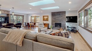 A modern living room with a sofa, a dining area, and a fireplace. - Beautiful home with private hot tub, gazebo, and gas fireplace (South Lake Tahoe)