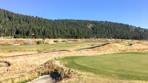 Een golfbaan met een heldere lucht, een beboste heuvel en een waterpartij.