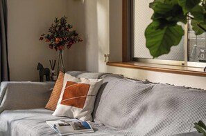 Un canapé avec un coussin, un magazine, une plante et une fenêtre donnant sur un beau paysage.