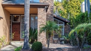 Ein Haus mit Steinaußenwand, einer Holztür und einem gepflegten Garten mit Palmen und Sträuchern.