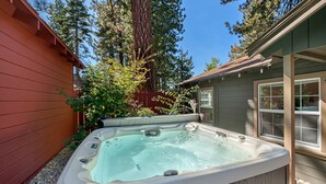 Ein Whirlpool in einem Garten mit Holzzaun, einem Haus und hohen Bäumen.