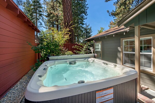 Un bain à remous dans un jardin, avec une clôture en bois, une maison et de grands arbres.