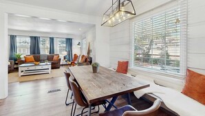 Ein modernes Wohnzimmer mit einem Holzesstisch, bequemen Sitzgelegenheiten und einem großen Fenster mit Jalousien.