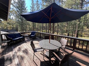 Une terrasse en bois, aménagée avec du mobilier d’extérieur, notamment une table et des chaises, et un grand parasol pour créer de l’ombre.