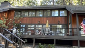 A two-story building with a wooden exterior, a balcony with outdoor furniture, and an American flag. - Golf-course-front home with great deck, game room, fireplace & forest views (Incline Village)