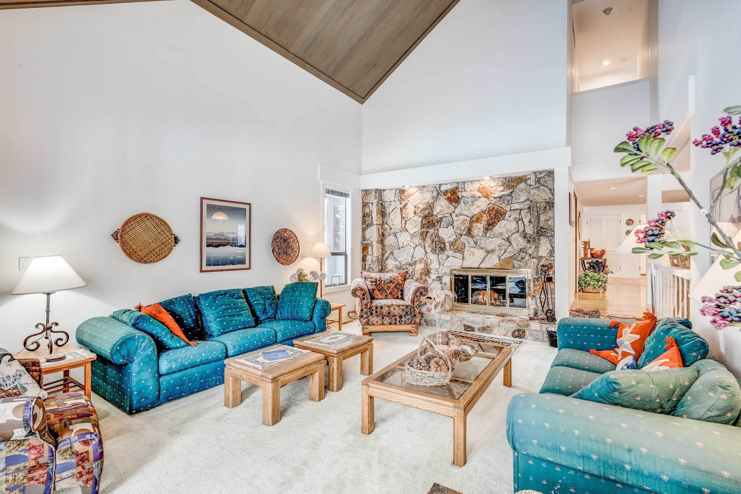 Een ruime woonkamer met een stenen openhaard, een blauwe zithoek, houten salontafels en uitzicht op het interieur door een open deur.