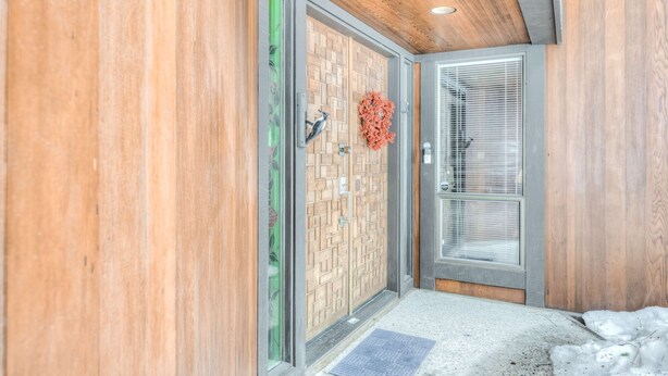 A modern entrance with wooden paneling, a glass door with a metal handle, and a decorative wreath. - Golf-course-front home with great deck, game room, fireplace & forest views (Incline Village)