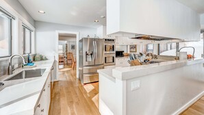 A modern kitchen with stainless steel appliances, a central island, and a view into the dining area. - Golf-course-front home with great deck, game room, fireplace & forest views (Incline Village)