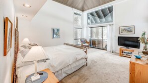 A bedroom with a bed, bedside lamp, TV, and a view of the outdoors. - Golf-course-front home with great deck, game room, fireplace & forest views (Incline Village)