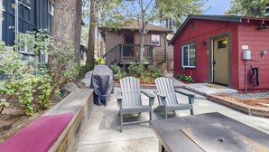 Een woonhuis met een overdekte patio, twee Adirondack-stoelen, een rood gebouw en een kleine schuur.