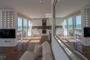 Uma sala de estar ampla com uma televisão de tela plana grande, um sofá e uma varanda com vista para o oceano.