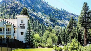 Squaw Valley Lodge med en bergskuliss i bakgrunden, en inhägnad trädgård och en klar himmel.