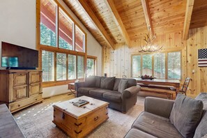 Un salón amplio con un techo de madera grande, un televisor, un sofá, una mesa de centro y ventanas grandes.