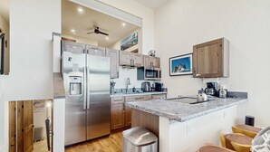 A modern kitchen with stainless steel appliances, wooden cabinets, a granite countertop, and a small island with stools. - Luxury Condo in Stateline: Lake & Mountain Views (Stateline)