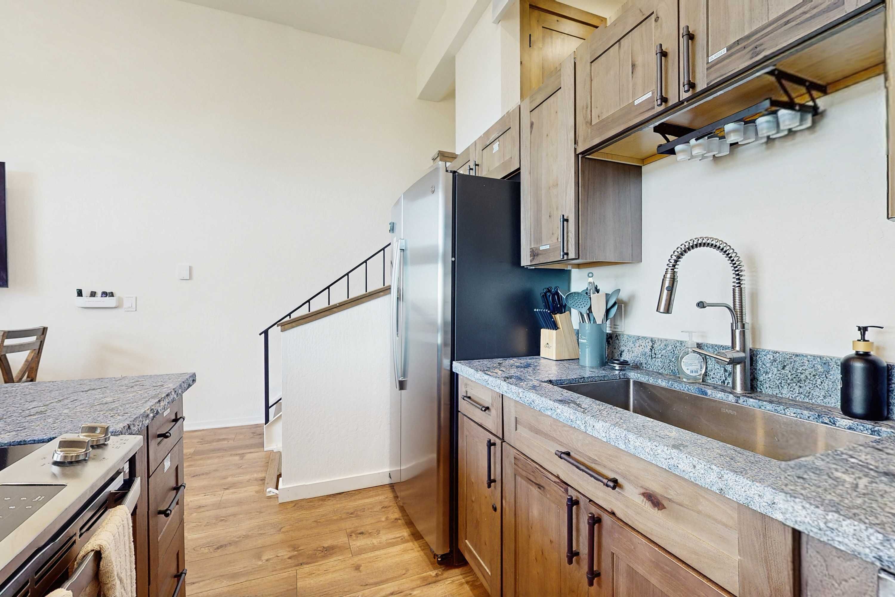 A kitchen with wooden cabinets, a stainless steel refrigerator, a granite countertop, and a built-in oven.