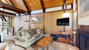 Ein Wohnzimmer mit Holzboden, einer Couch, einem Couchtisch, einem Fernseher und einem Kamin.
