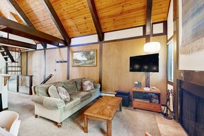 Ein Wohnzimmer mit Holzboden, einer Couch, einem Couchtisch, einem Fernseher und einem Kamin.