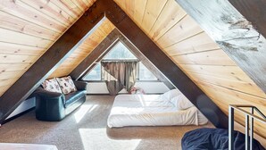 Ein Schlafzimmer im Dachgeschoss mit schrägen Wänden, einem Bett, einer Couch und einem Fenster.