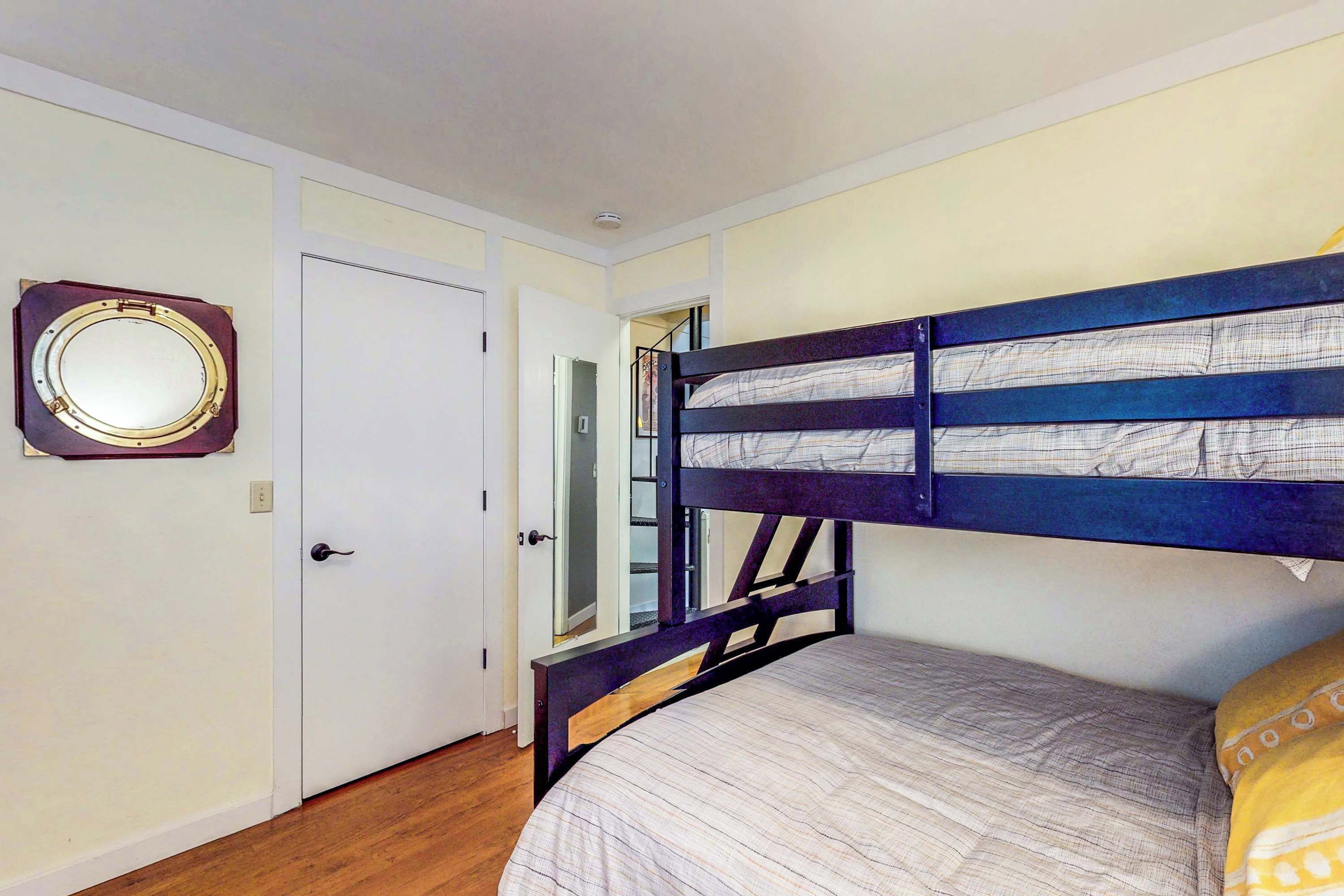 Uma cama de solteiro com cabeceira, uma porta com espelho e uma escada que dá acesso a um andar superior.
