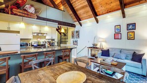 Uma cozinha ampla com vigas de madeira, uma sala de jantar com mesa de madeira e uma sala de estar com sofá e obras de arte na parede.