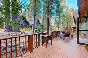 A wooden deck with outdoor furniture, surrounded by trees and a stone wall. - Chalet-style Townhome with Fireplace, Deck, Near Ski Resort, Incline Village (Incline Village)