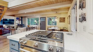 Una cocina moderna con una estufa grande, techo de madera y un comedor con televisor.