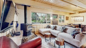 Una sala de estar con sofá modular, chimenea, televisor y comedor con piano.