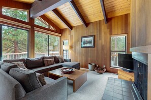 A modern living room with a sectional sofa, a coffee table, a fireplace, and large windows. - Serene home with fireplace, spacious deck, sauna, WiFi and nearby activities (Truckee)