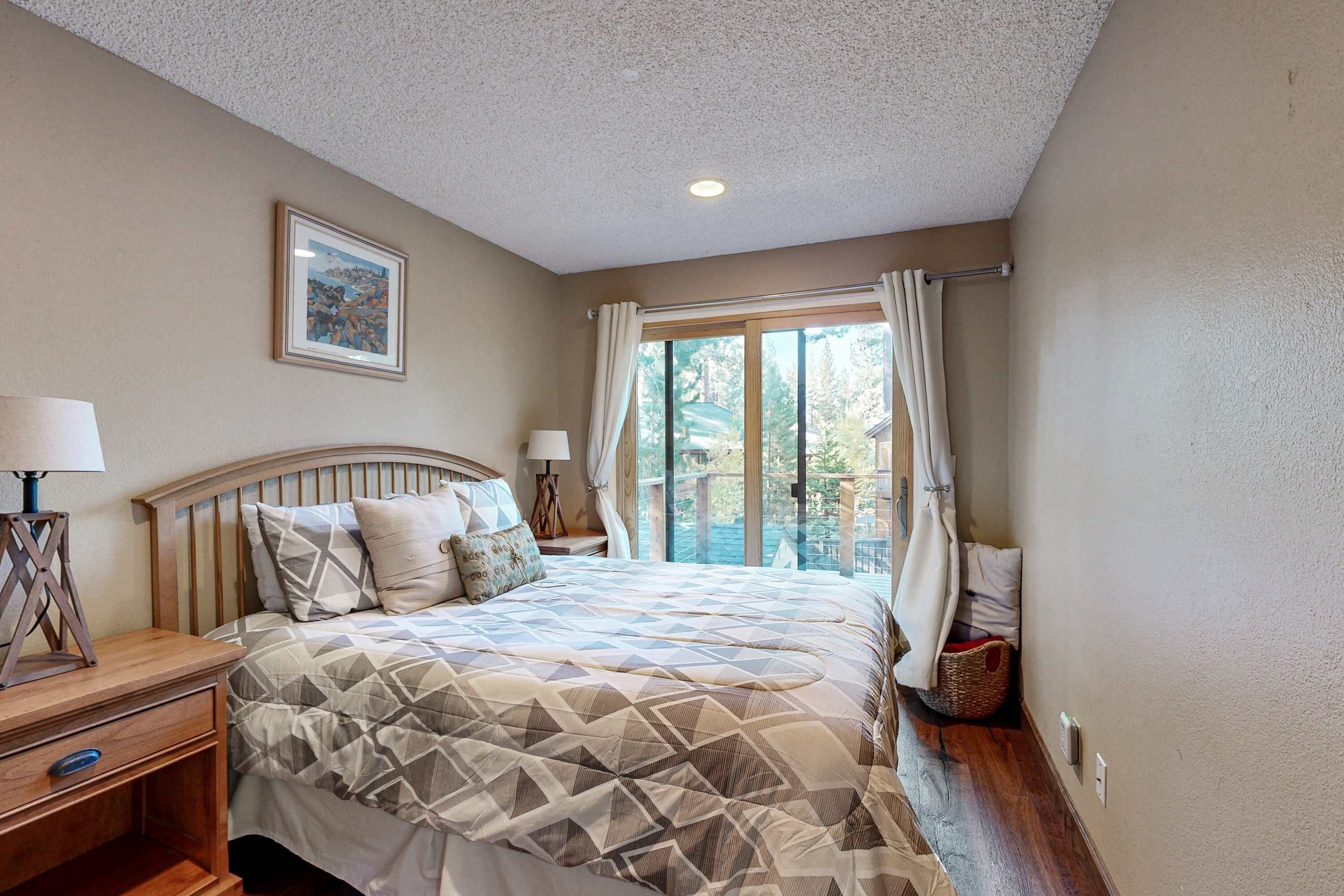 A bedroom with a bed, nightstands, a window with curtains, a framed picture on the wall, and a wooden floor.