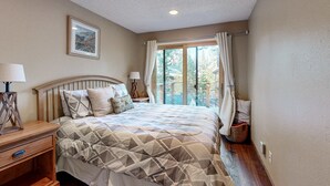 Un dormitorio con cama, mesitas de noche, una ventana con cortinas, un cuadro enmarcado en la pared y suelo de madera.